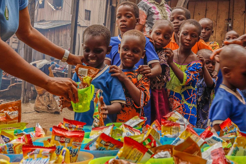 a-boy-holding-a-green-cup-9090750 Joyful children receiving food supplies from a volunteer in an outdoor setting.