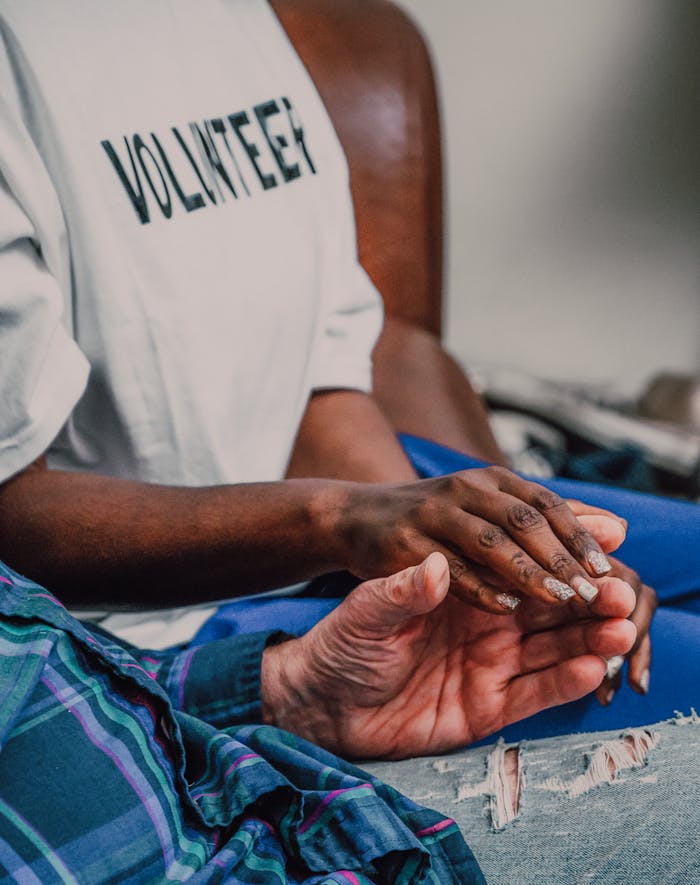 man-in-white-t-shirt-and-blue-pants-6646816 A volunteer offering comfort by holding hands with an elderly person, showcasing compassion.