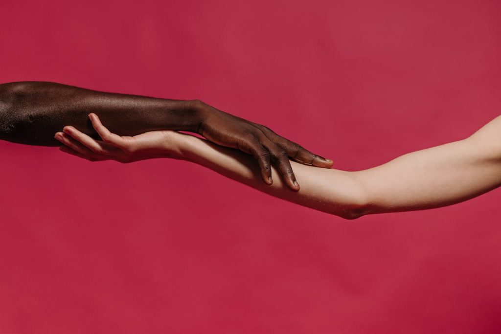 people-holding-each-other-s-arm-near-red-wall-9486843 Embrace of two diverse hands against a vibrant red backdrop symbolizing unity.