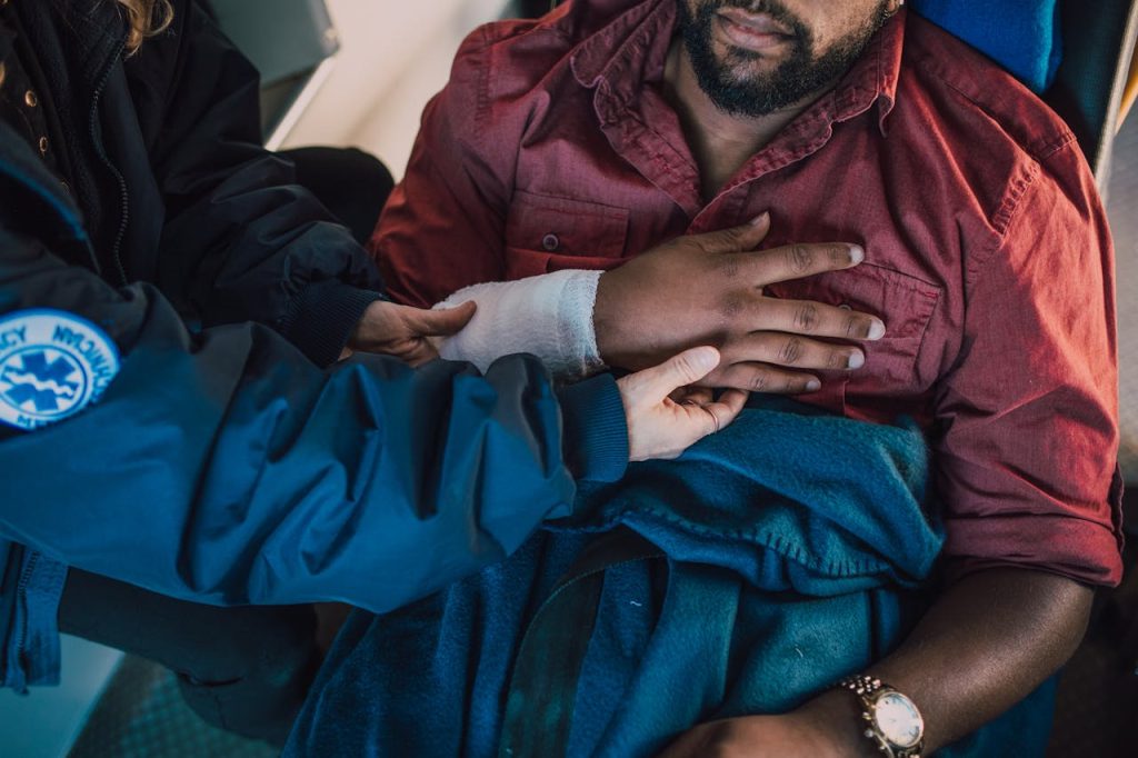 person-helping-a-man-place-his-arm-on-chest-6520100 Paramedic assisting injured patient with arm bandaged in an emergency scenario.