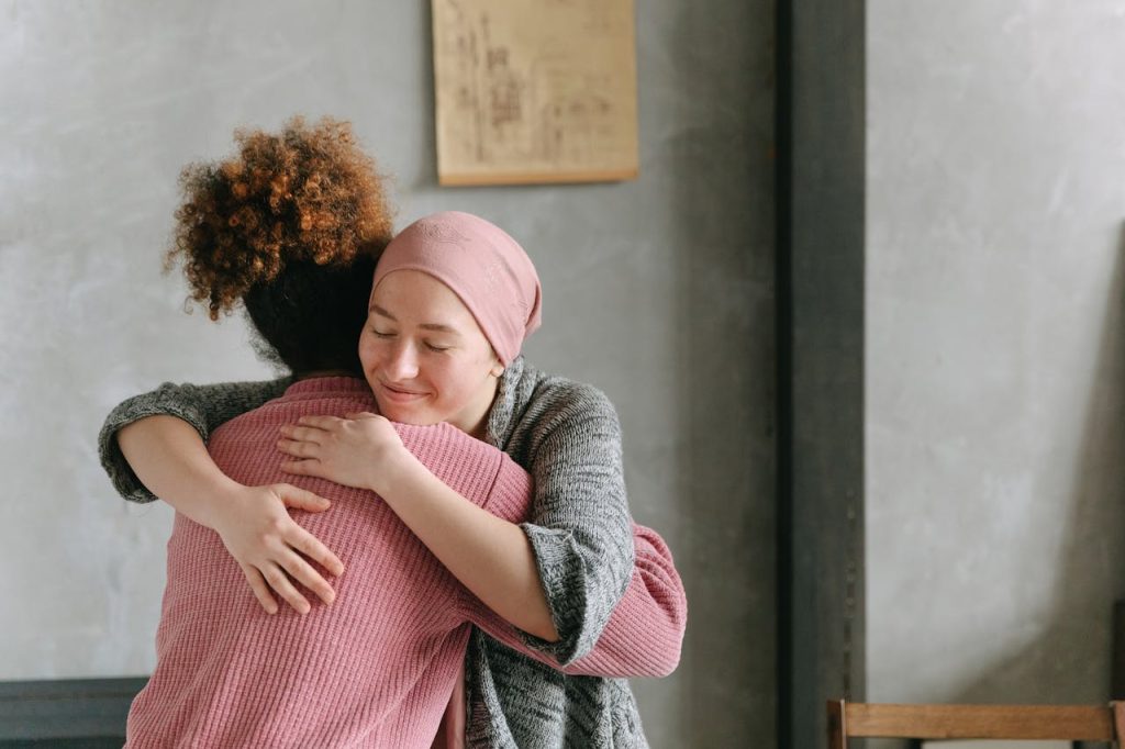 women-hugging-each-other-7659454 Two women embracing each other with warmth and love, symbolizing support and care indoors.